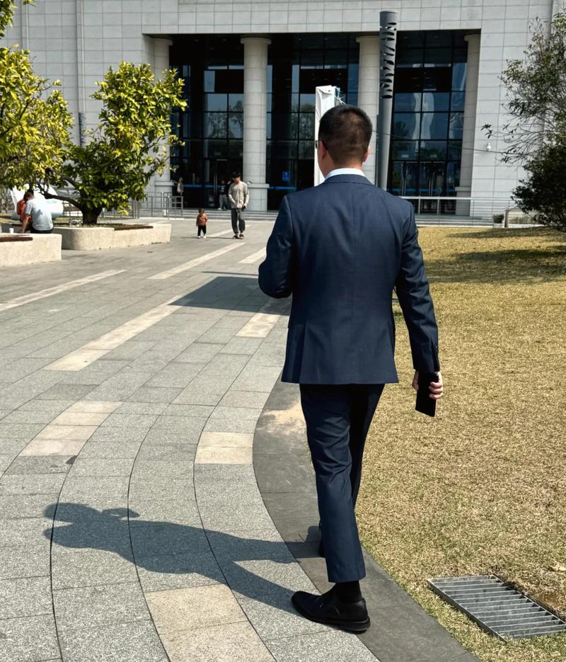 火车站台一个西装男人低头剥橘子的侧影，背景模糊人流