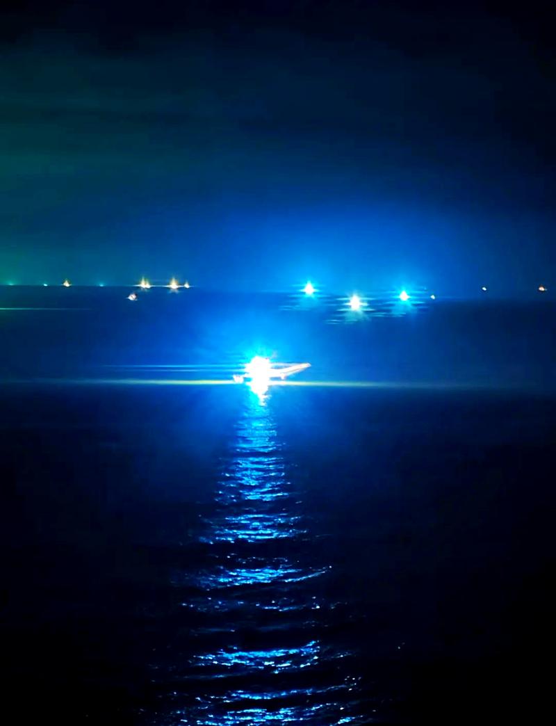 夜晚大海中孤独发光的灯塔，远处有渔船