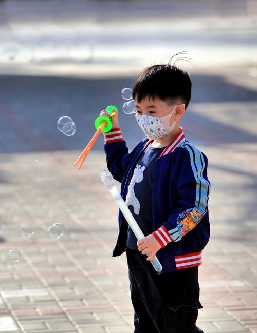 小男孩拿着泡泡机对着窗外吹泡泡做呼吸练习的实拍图