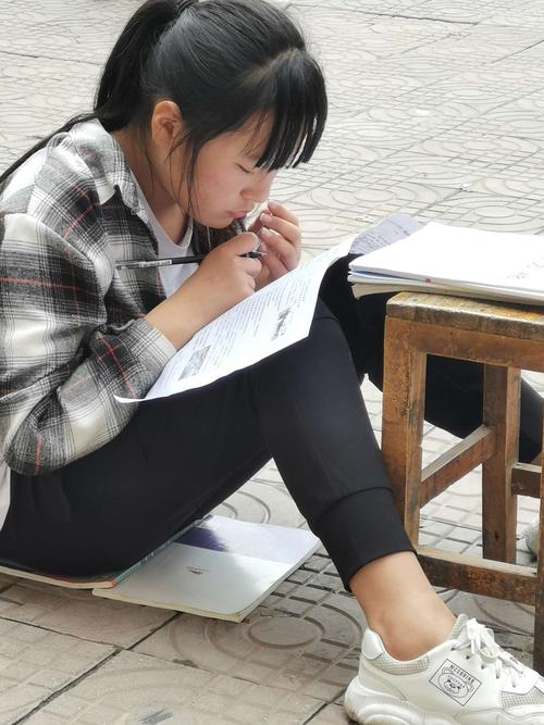 学生在走廊台阶上对着横线笔记本写字的侧影