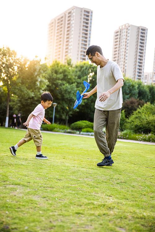 公园草坪上父亲陪孩子滚草地玩耍