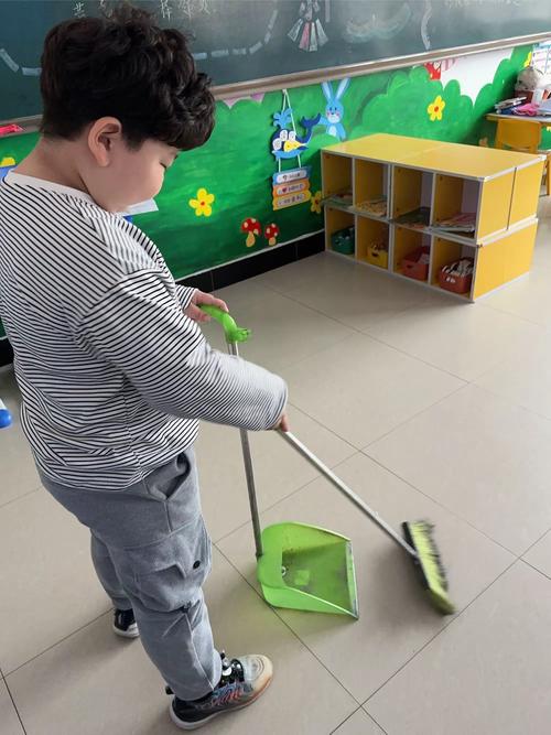 幼儿拿着小扫帚模仿大人扫地场景