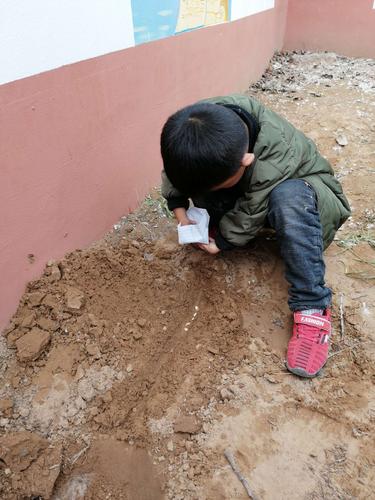 小区楼下儿童蹲在土坡上观察土壤断面