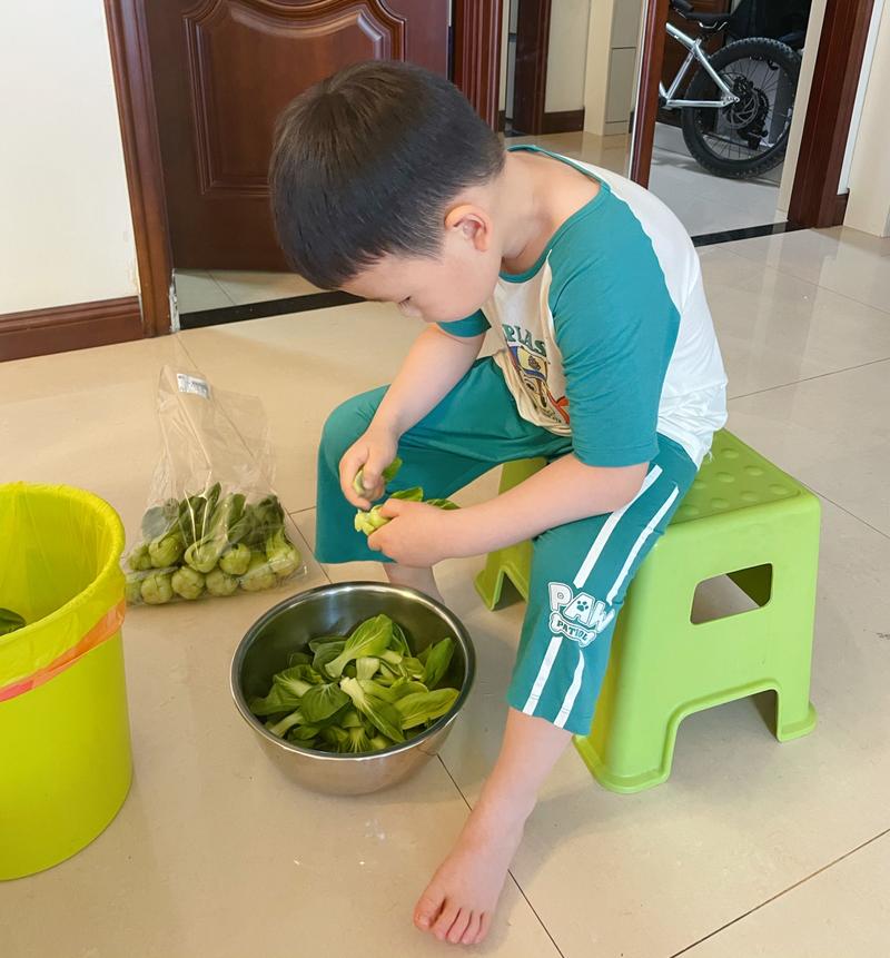 孩子在厨房小梯凳上参与摘菜洗菜的居家场景