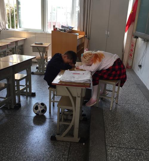 小学班主任蹲在课桌旁和抠橡皮的小男孩聊天的实拍图