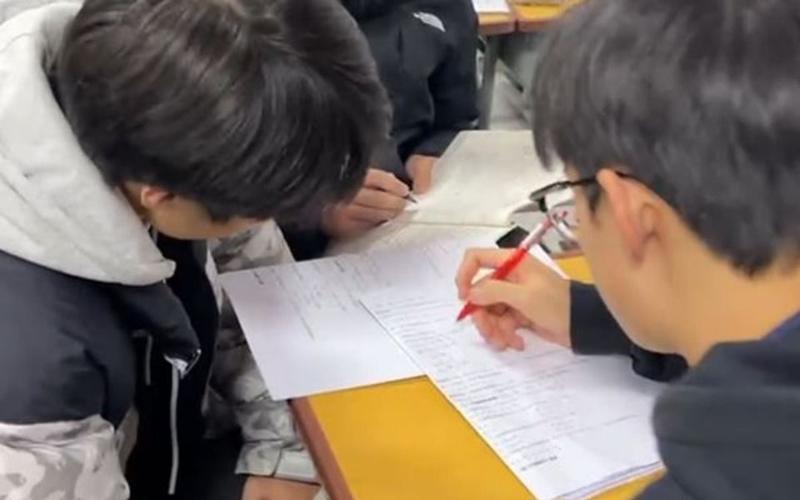 中学生课间围着老师指着练习册上的错题提问