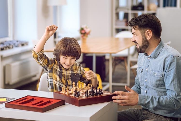 父亲紧紧拥抱情绪低落的小男孩，男孩手握棋子