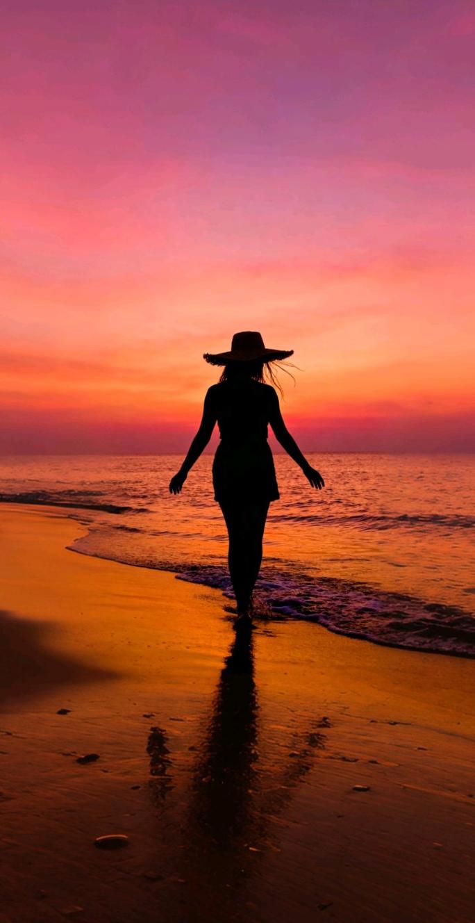 海边夕阳下戴着宽檐草帽的女子背影