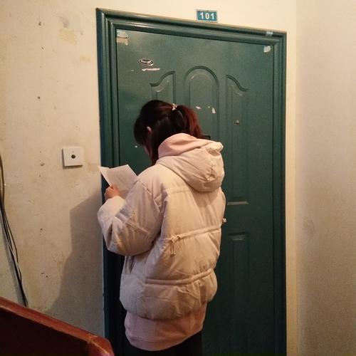 教师站在老式居民楼三楼防盗门前攥着皱作业袋的场景