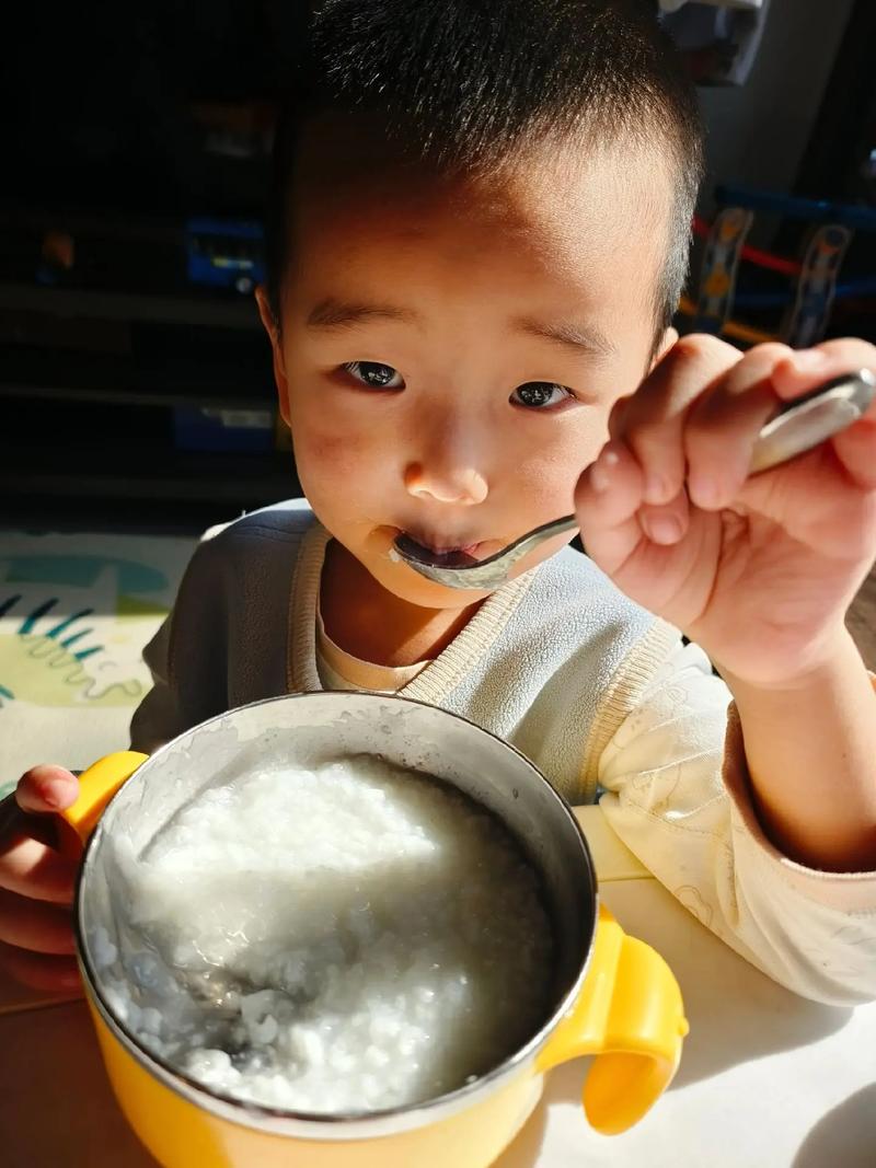 普通家庭餐桌上小孩自己拿勺子喝粥