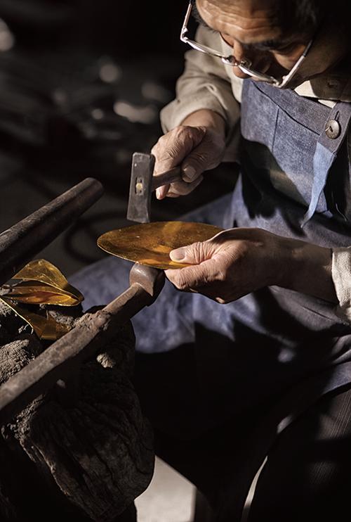 老工匠在金属工件上手工钻孔并浇注菜油降温