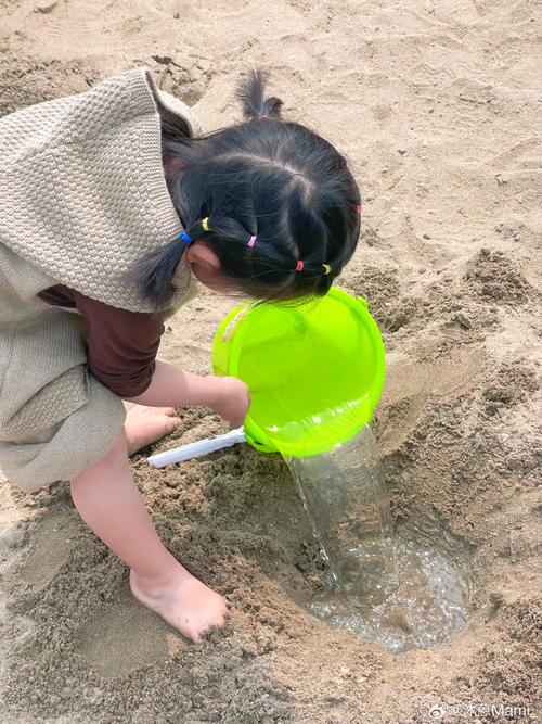 孩子蹲在沙坑里用小桶倒沙土的特写照片
