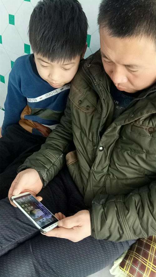 少年宫门口靠墙刷手机的年轻父亲