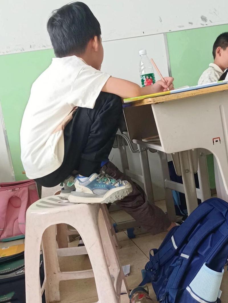 六岁刚上小学的孩子坐教室课桌前不安抠手