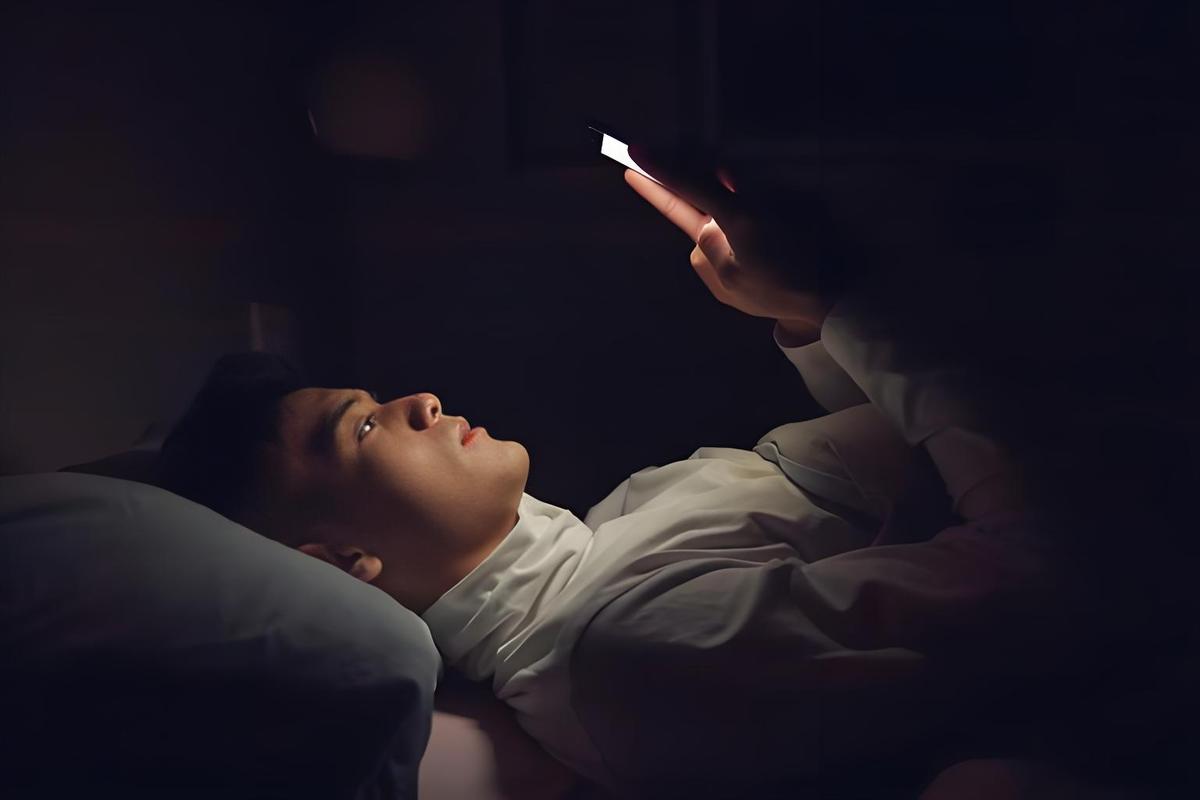 一个男人深夜独自坐在床边低头看手机,屏幕的微光映出他脸上的困惑,卧室背景昏暗,隐喻亲密关系中的孤独感