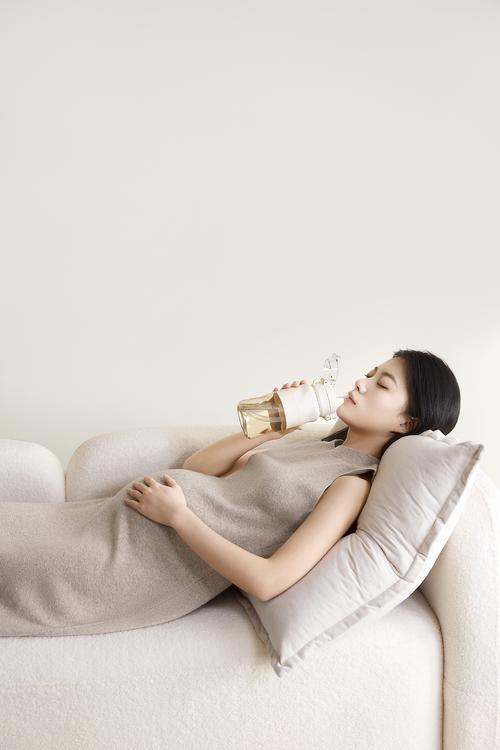 经期女性靠在沙发上盖针织毯喝温饮