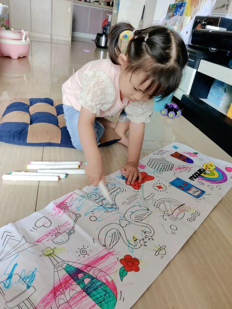 2岁幼儿趴在客厅地板上用粗蜡笔在大张画纸上乱涂的实拍图
