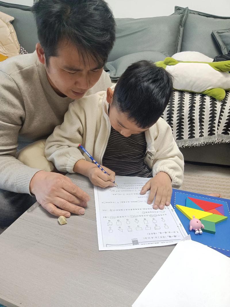 穿藏青色工装的爸爸在家陪六岁儿子握铅笔写数字的居家实拍