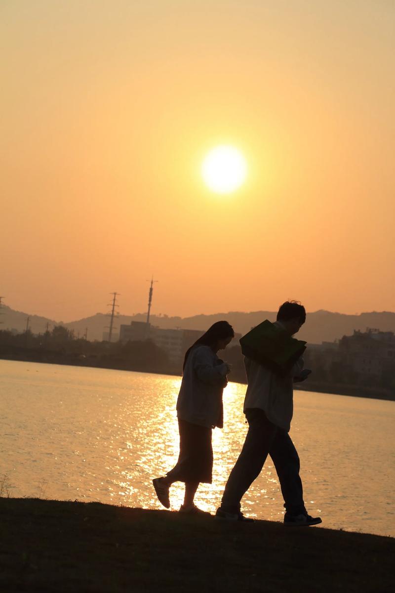 夕阳下波光粼粼的湖面与散步的人影