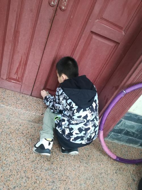 小男孩站在单元门门口攥着衣角躲邻居问话的实拍图