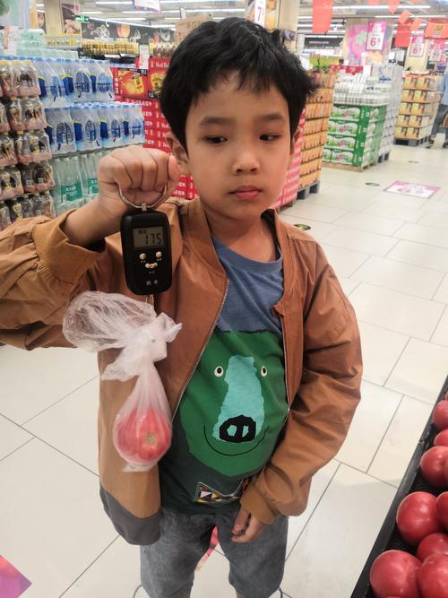 家长和孩子在小区菜市场拿着迷你弹簧秤称西红柿