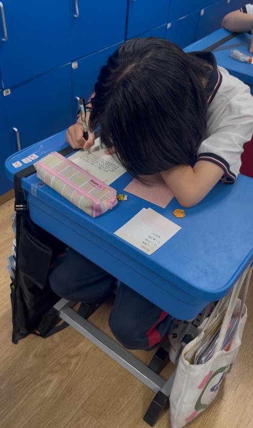 中学教室靠窗座位学生低头抠笔袋场景
