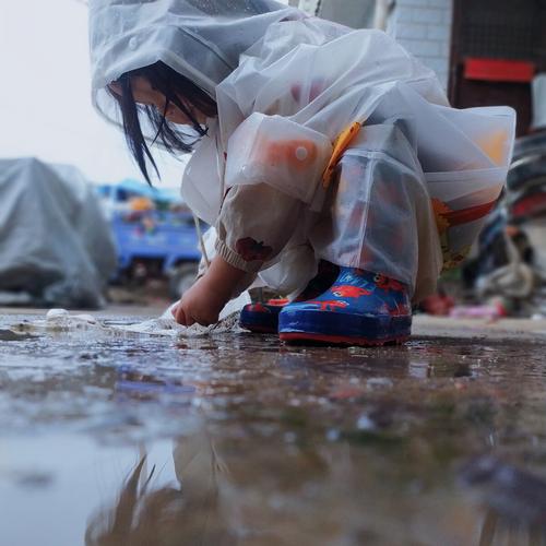 小孩蹲在公园路边观察雨水冲出的沙沟