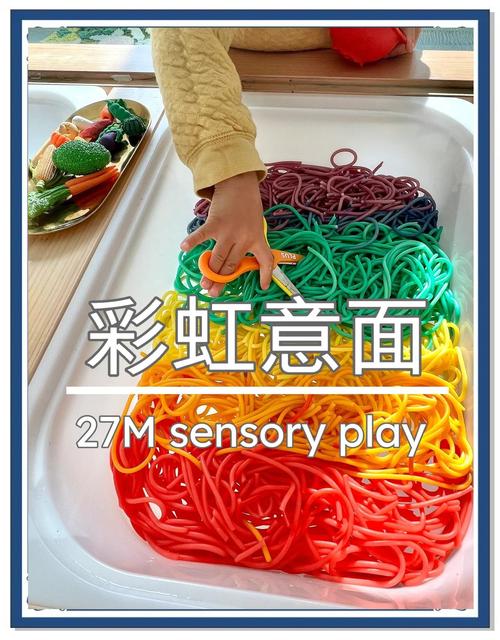 幼儿坐在地板上玩彩色意面感官盆