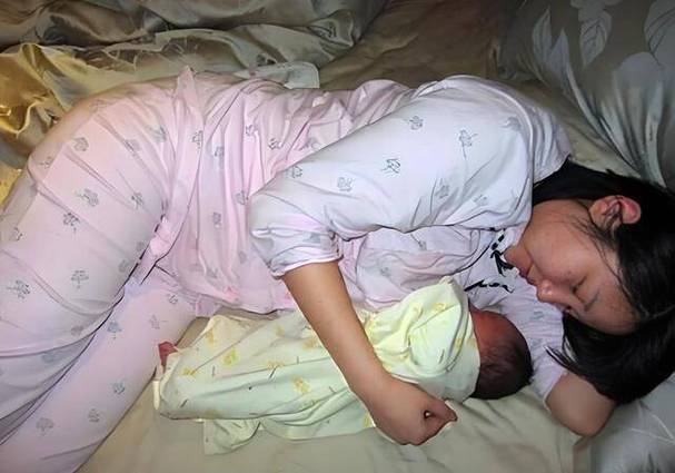 妈妈侧身抱着婴儿一起躺在床上的温馨画面