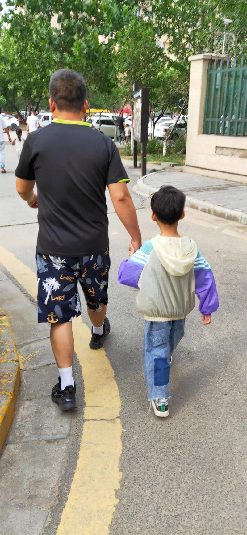 父亲在远处看着孩子独自背书包上学的背影
