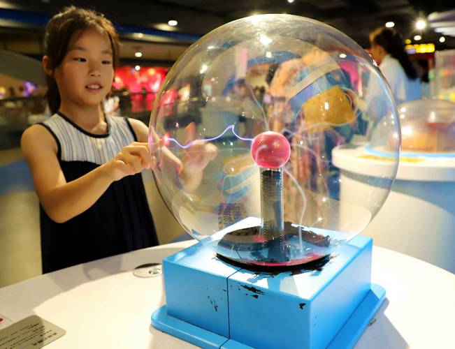 科技馆里一个小孩正在触摸巨型全息地球模型，眼中倒映着光