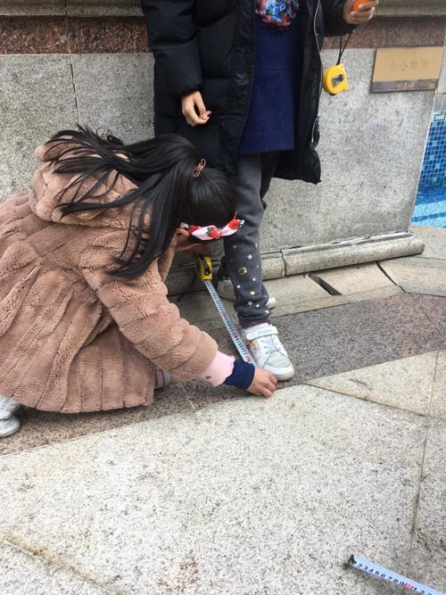 小学生蹲在小区人行道边测量地砖长度