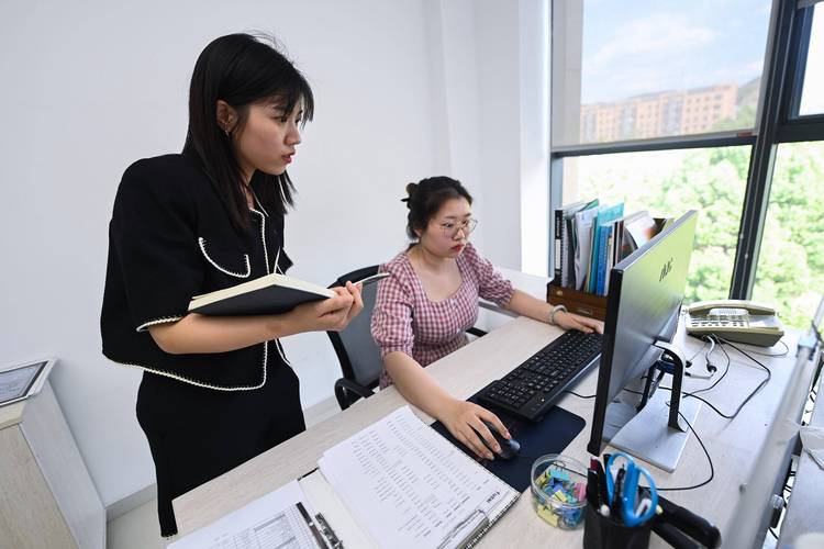 职场新人抱着笔记本在工位上向前辈请教问题的实拍