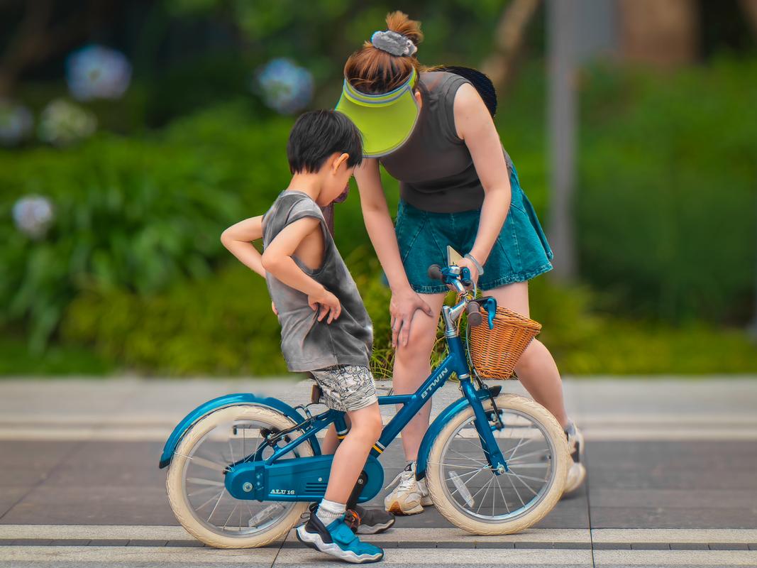 妈妈蹲在路边看孩子学骑自行车的实拍图