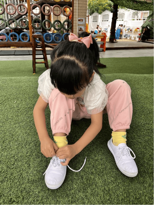 孩子蹲在地上认真系鞋带背影照片