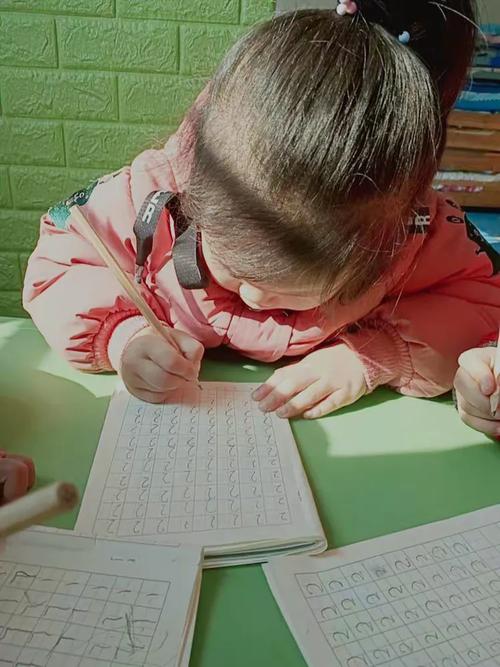 幼儿园大班孩子趴在桌前写田字格生字的真实场景