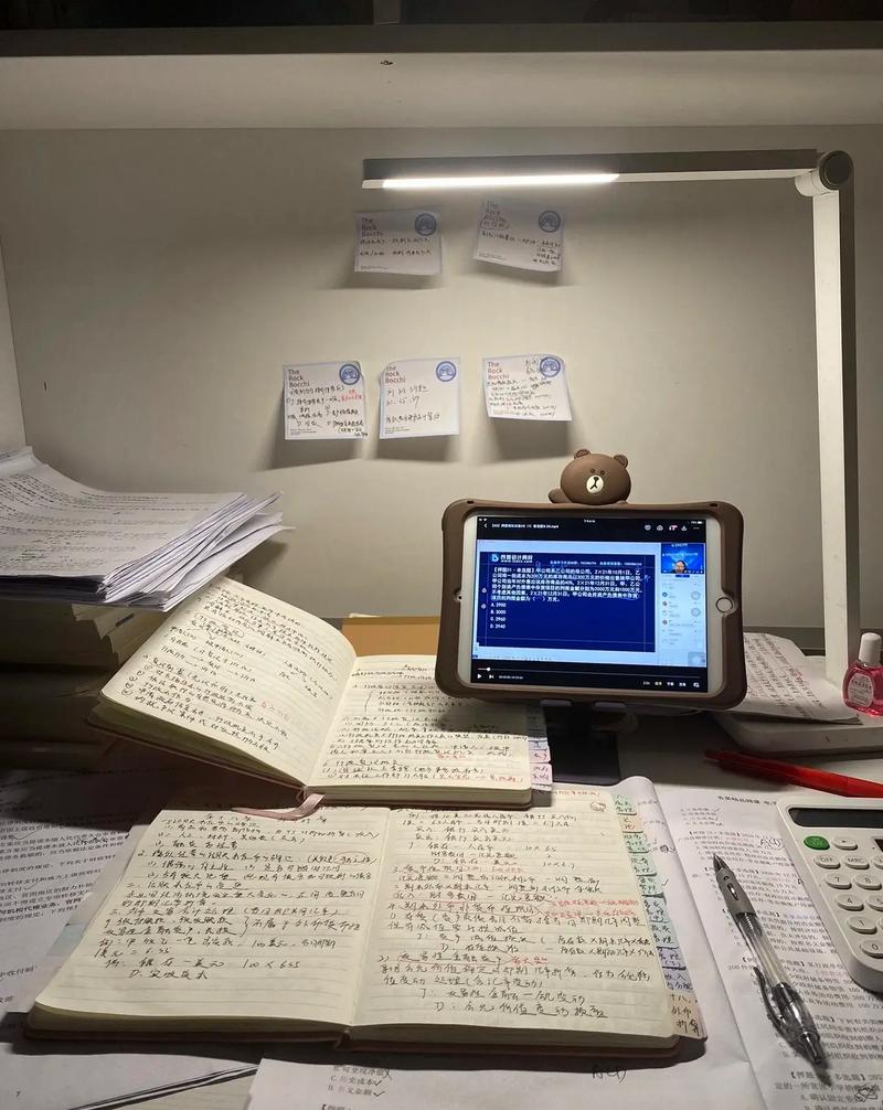 一建备考书桌场景，堆满教材和规范，荧光笔划重点，旁边放着一台笔记本电脑