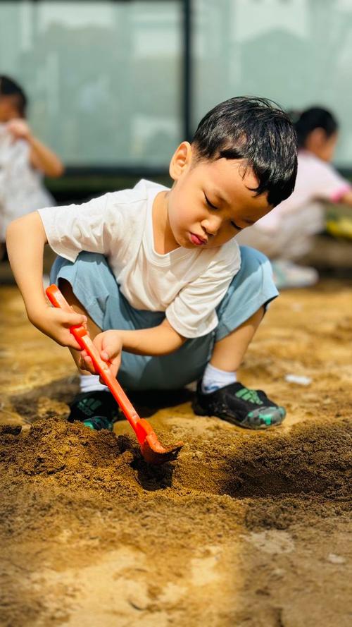 小男孩蹲在小区沙坑专注挖沙的实拍图