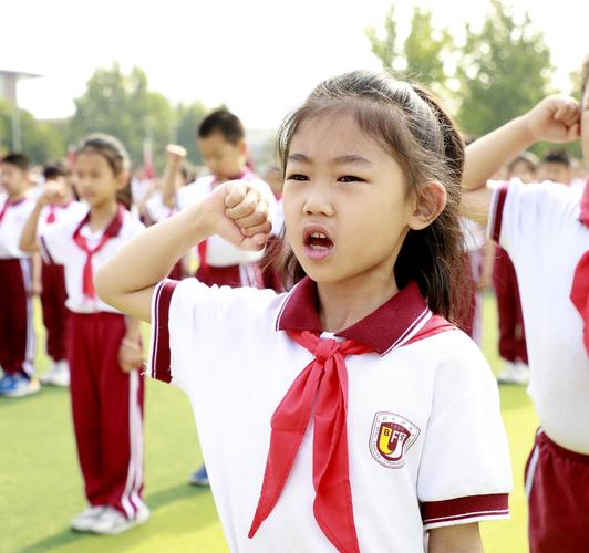 一群小学生戴着红领巾在大学校门前合影,表情无趣