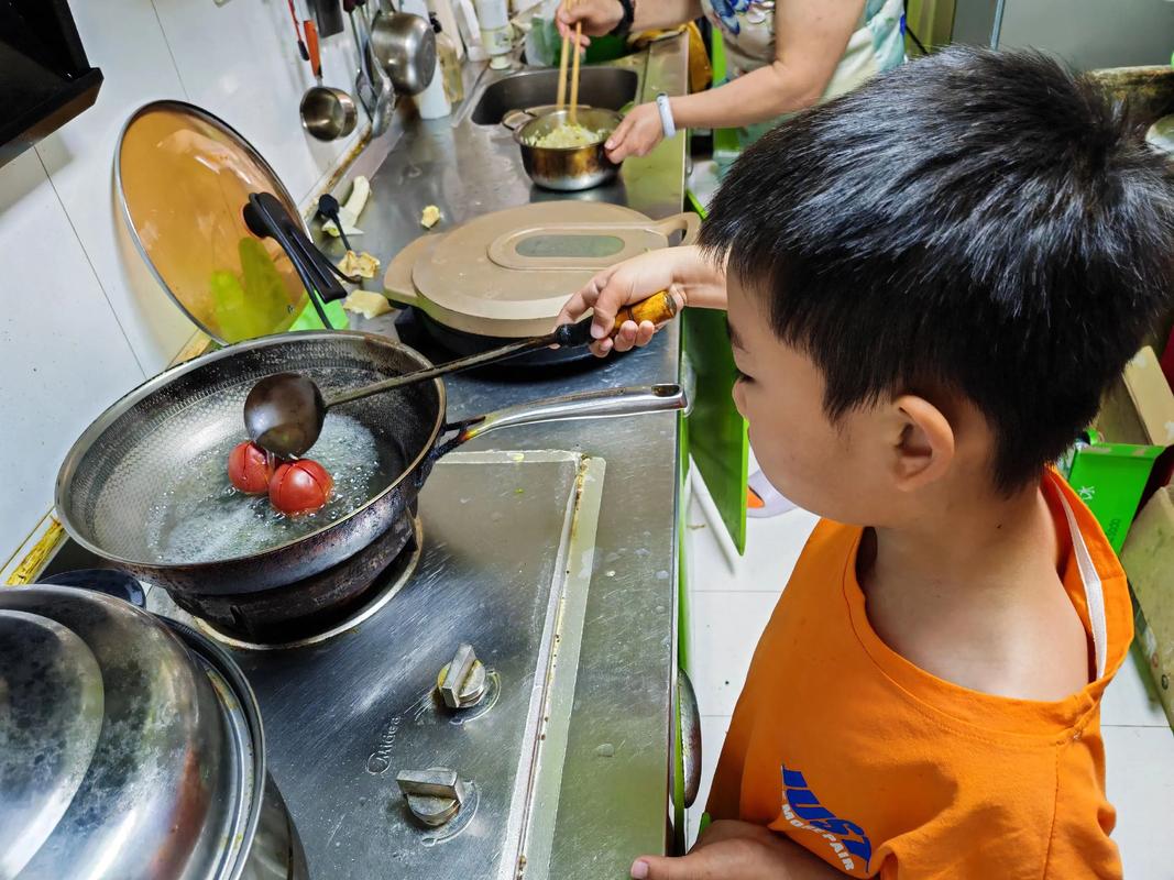 孩子站在小凳上炒菜锅里西红柿鸡蛋炒糊了