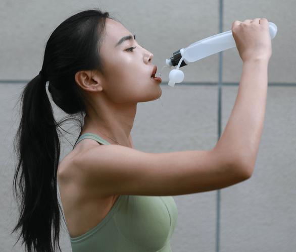 户外跑步后女性拿着水壶小口喝水