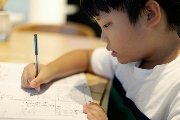 小学生独自坐在书桌前翻数学书找例题的侧影