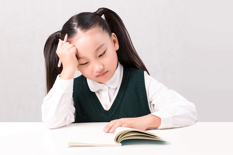 小学女孩独自坐在书桌前对着练习册发呆的特写