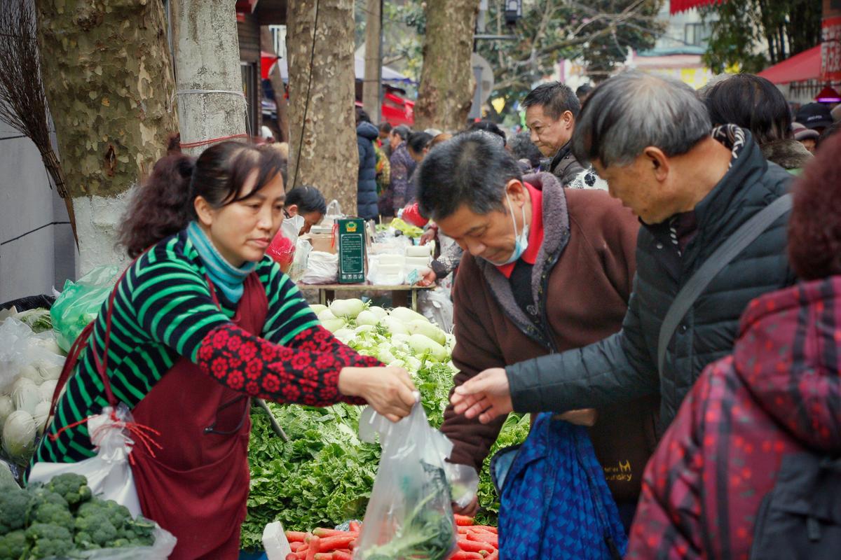 菜市场摊主举着新鲜蔬菜跟顾客搭话的日常场景