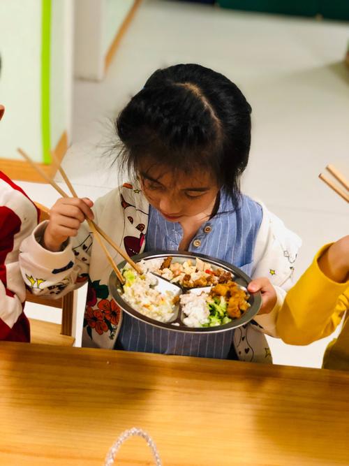小孩踩着小凳子在餐桌边端自己的饭碗