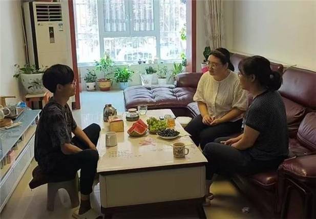 老师坐在居民家客厅沙发上 跟老人和孩子一起吃西瓜