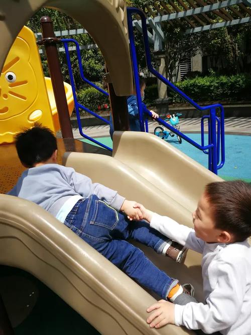 小区滑梯边两个牵手对视的小男孩