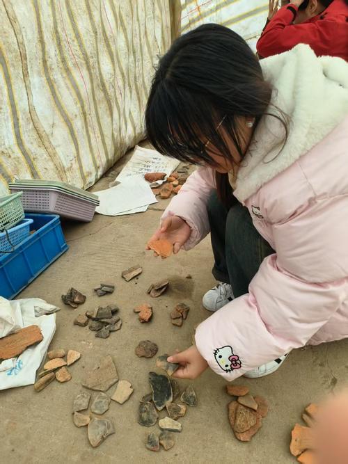 学生在古窑址遗址蹲在地上观察碎瓷片的场景