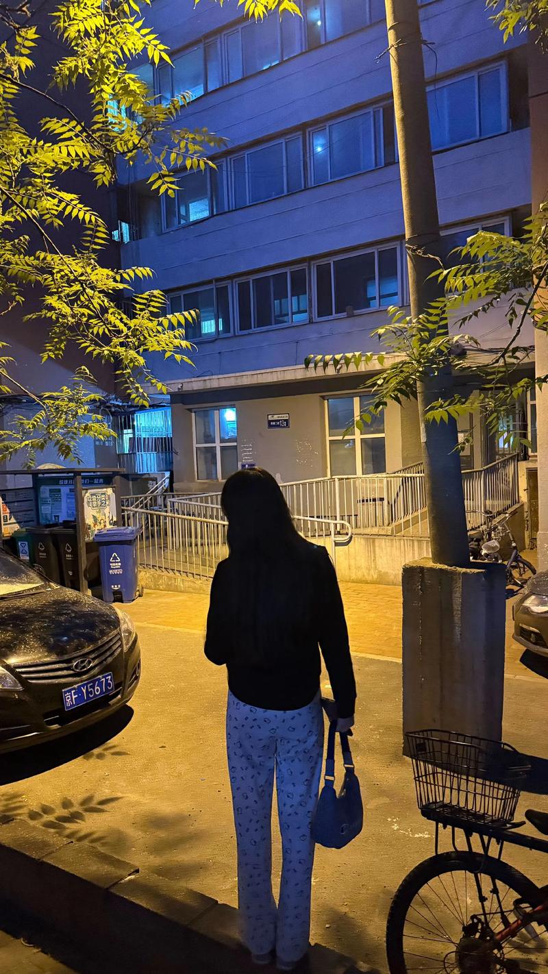 夜晚小区单元门靠墙站着的女生背影