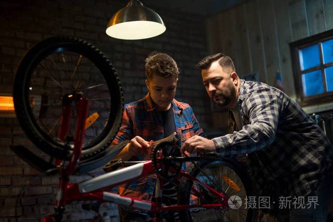 父子在车库里一起修理旧自行车,孩子递工具